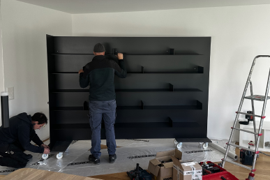 Installation sur site d’une bibliothèque en alu noir mat réalisée sur mesure, pose en cours dans la future zone bibliothèque.