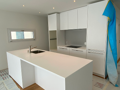 Cuisine blanche sur mesure avec grand îlot central et évier intégré, installation en cours sur chantier