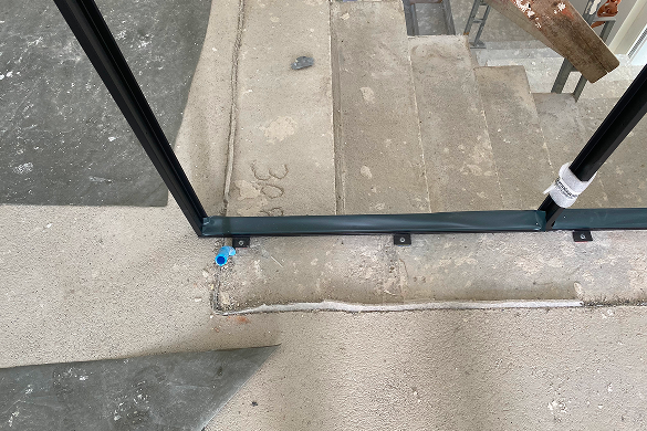 Détail de fixation au sol d’une verrière intérieure en structure acier noire sur chantier