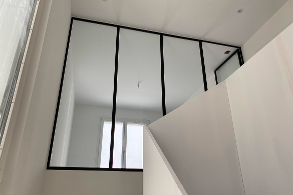 Verrière intérieure en acier noir installée au-dessus d’un escalier pour apporter de la lumière